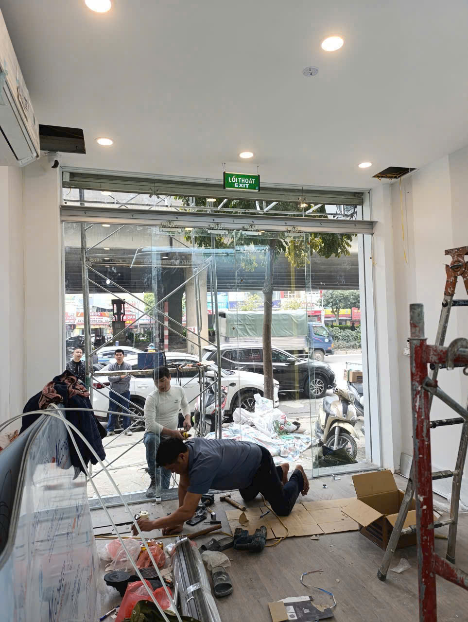 Thi công lắp đặt cửa kính cường lực mặt tiền cửa hàng với thợ đang làm việc trên sàn